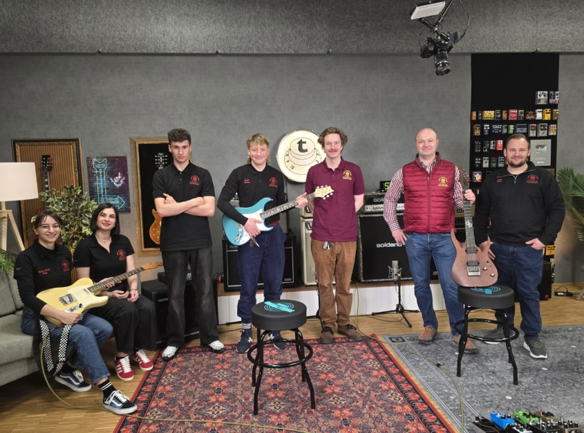 Ein Gruppenbild mit fünf Azubis und zwei Ausbildungskoordinatior:innen in einem Tonstudio mit drei E-Gitarren.