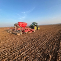 Ein Traktor auf einem Feld mit einer Sämaschine und blauem Himmel