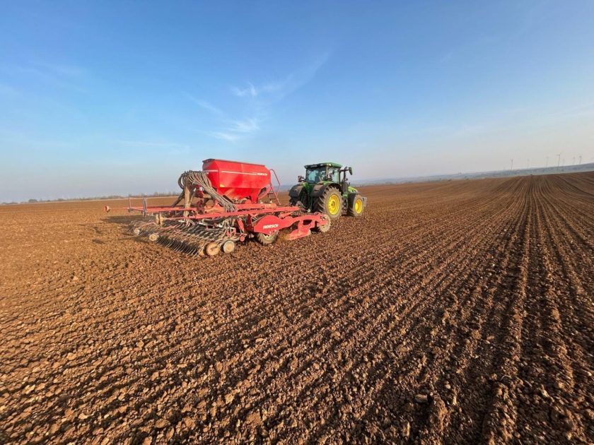Ein Traktor auf einem Feld mit einer Sämaschine und blauem Himmel