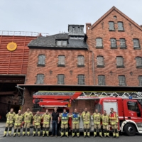 Gruppenbild der Feuerwehr in Montur mit Weyermann Mitarbeitenden vor Weyermann Gebäude und Feuerwehrauto