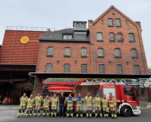 Gruppenbild der Feuerwehr in Montur mit Weyermann Mitarbeitenden vor Weyermann Gebäude und Feuerwehrauto
